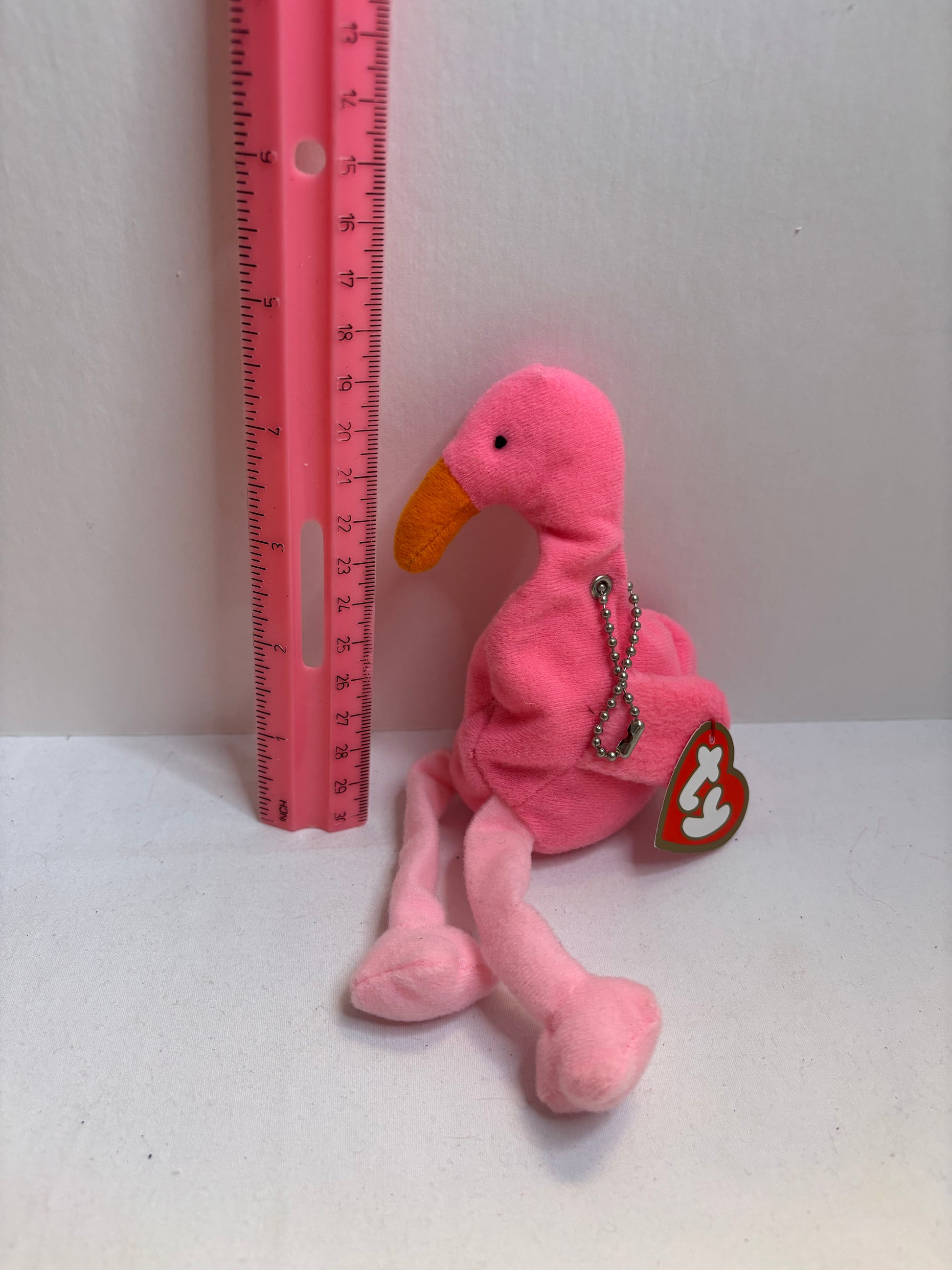 Pink flamingo plush bag charm with a tag on a white background