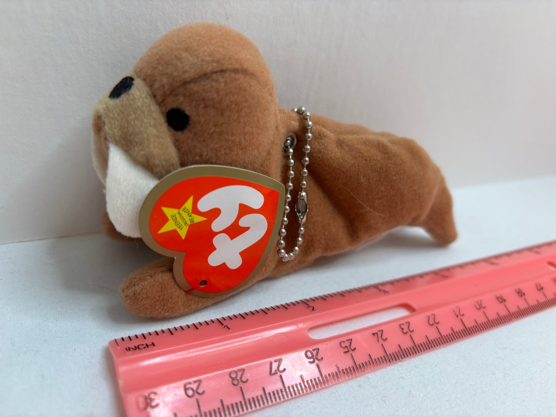 Brown plush walrus bag charm with a red tag on a white background