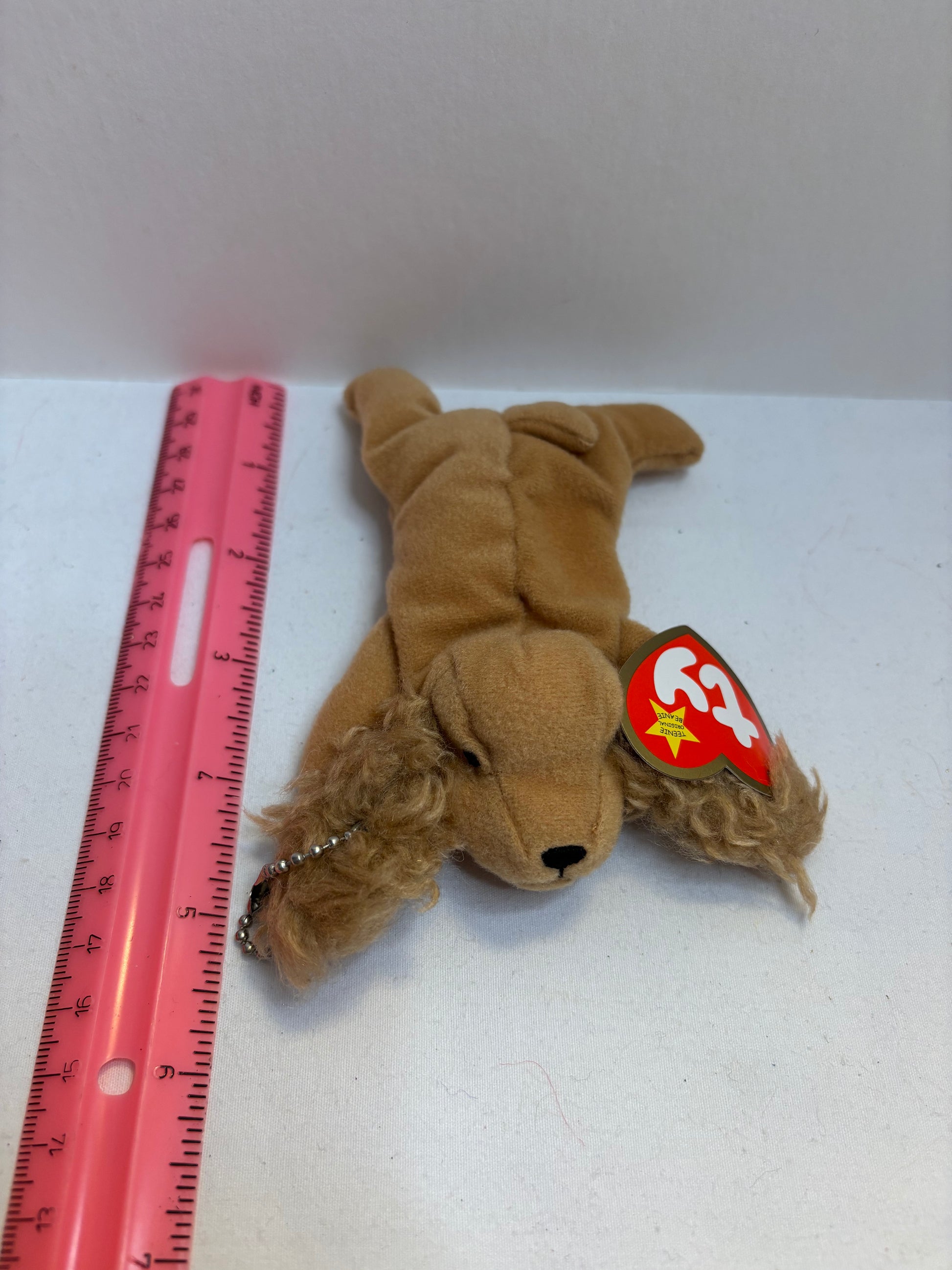 Brown plush dog bag charm with a red and yellow tag on a white background