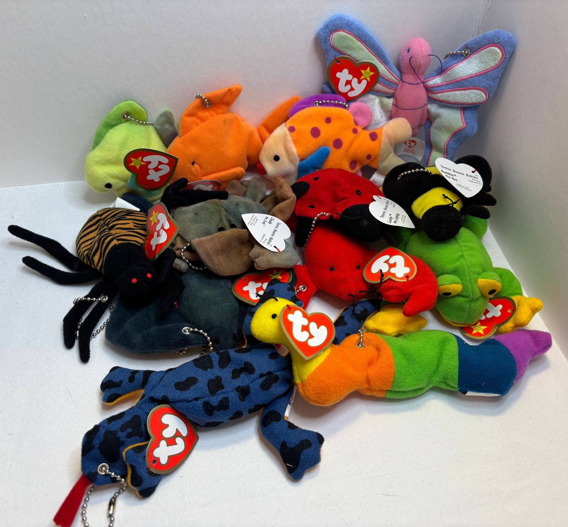 assorted colorful beanie baby plush toy bag charms in a pile on a white background